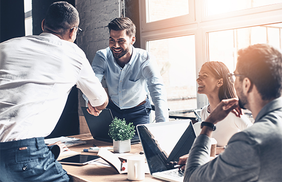 Glad to work with you! Young modern men in smart casual wear shaking hands and smiling while working in the creative office